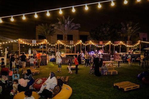 Evening community event with festoon lighting on a lawn at Al Zahia